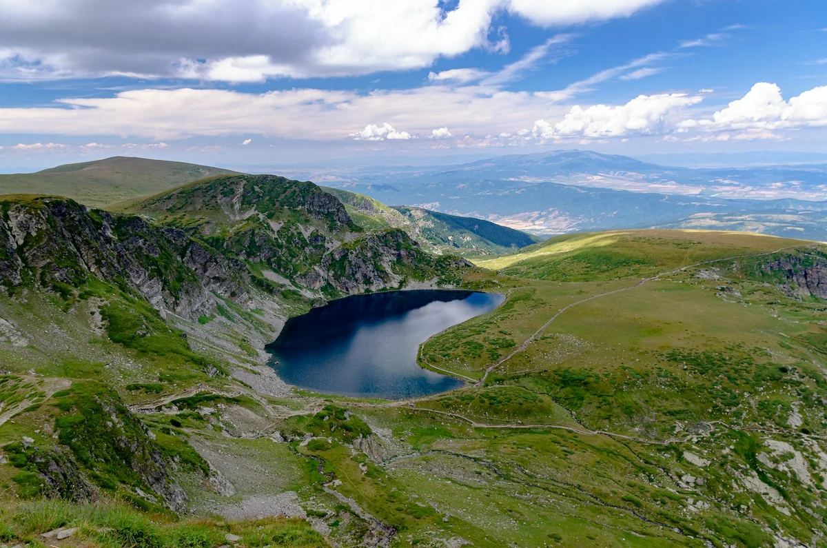 The kidney-shaped Babreka Lake surrounded by alpine grass and marked hiking trails in the Rila Mountains